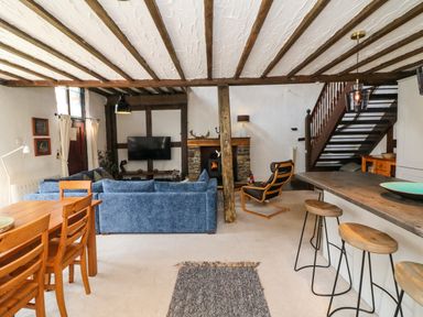 An open living room with blue sofas a wooden dining table a stone fireplace and a staircase at The Old Smithy in Lynton