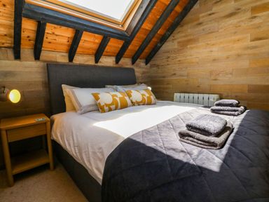 A bedroom with a bed pillows bedside table and folded towels by a skylight window at The Old Smithy in Lynton