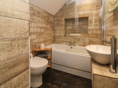 A bathroom with a toilet bathtub sink and wooden shelves at The Old Smithy in Lynton