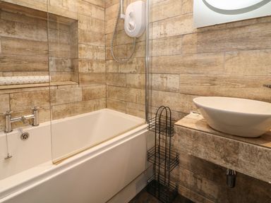 A bathroom with a bathtub shower combination a white sink and a black metal shelf at The Old Smithy in Lynton