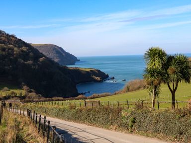 A coastal landscape with a path and fence leading to the sea with hills and trees at The Old Smithy in Lynton