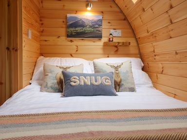 A wooden bedroom with a bed with cushions and a striped blanket at Caban Tirion in Dinas Mawddwy near Dolgellau