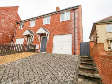A brick semi detached house with a driveway garage and stairs leading to a gate at Dotties Retreat in Weymouth