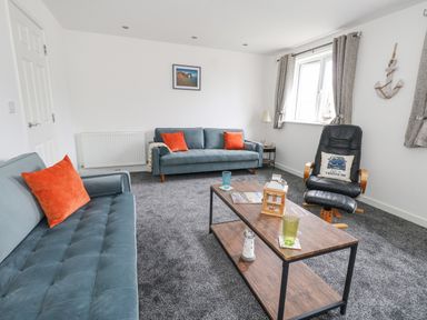 A living room with two blue sofas with orange pillows a black armchair a wooden coffee table with glasses and decor at Dotties Retreat in Weymouth
