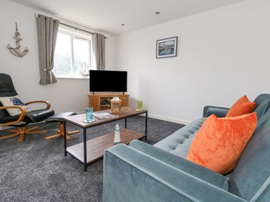 A living room with a blue sofa with orange pillows a wooden coffee table a black reclining chair and a television at Dotties Retreat in Weymouth