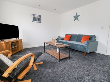 A living room with a blue sofa with orange cushions a wooden coffee table a black leather chair and a wooden TV stand at Dotties Retreat in Weymouth