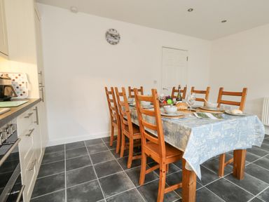 A dining area with a table set with plates and bowls surrounded by wooden chairs in a kitchen at Dotties Retreat in Weymouth