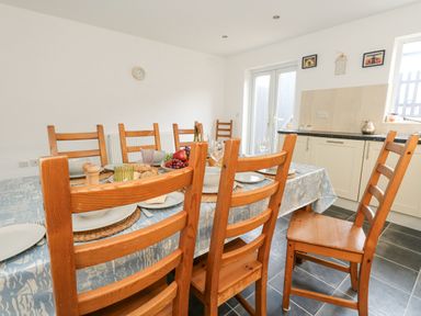 A dining table set with plates bowls and fruit surrounded by wooden chairs in a kitchen at Dotties Retreat in Weymouth
