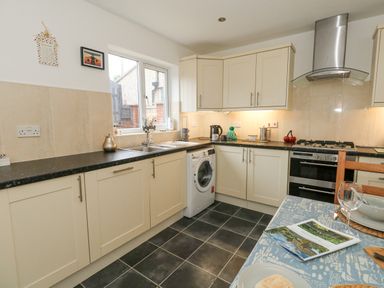 A kitchen with cream cabinets black countertops a washing machine stainless steel oven and a table set with dishes at Dotties Retreat in Weymouth