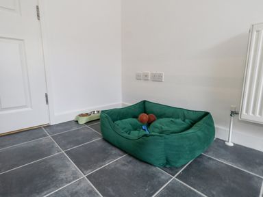 A pet bed with toys and a food bowl on a tiled floor near a white door and radiator at Dotties Retreat in Weymouth