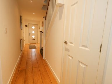 A hallway with wooden floor leading to a front door with diamond shaped windows and a carpet at Dotties Retreat in Weymouth