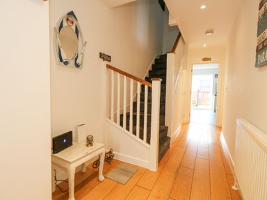 A hallway with wooden flooring stair railings and a small white table with objects at Dotties Retreat in Weymouth