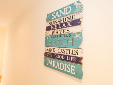 A wooden beach-themed wall sign with words like sand sunshine relax waves beach and paradise at Dotties Retreat in Weymouth
