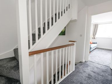 A carpeted staircase with white railings and wooden handrails leading to a room with a sofa and window at Dotties Retreat in Weymouth