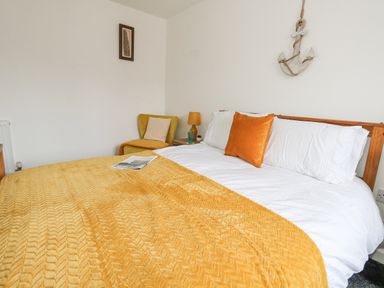 A bedroom with a bed covered by a yellow blanket and orange pillow a yellow chair and a wooden anchor on the wall at Dotties Retreat in Weymouth