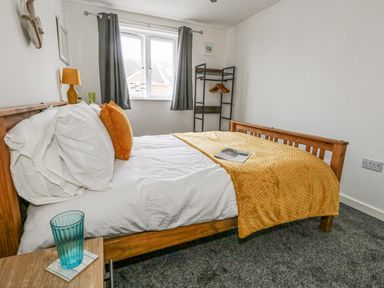 A bedroom with a wooden bed white sheets yellow blanket and orange pillows at Dotties Retreat in Weymouth