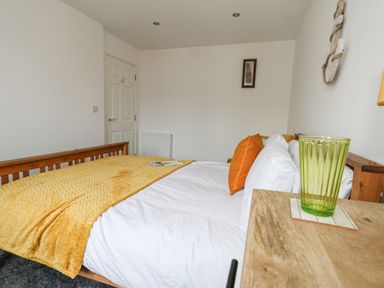 A bedroom with a wooden bed with white sheets and yellow blanket and orange cushions at Dotties Retreat in Weymouth