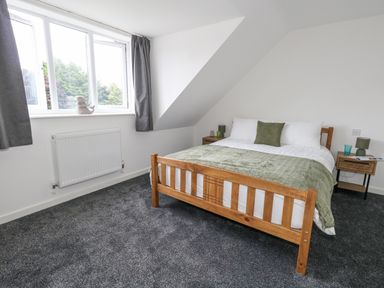 A bedroom with a wooden bed and green bedding next to two wooden bedside tables at Dotties Retreat in Weymouth