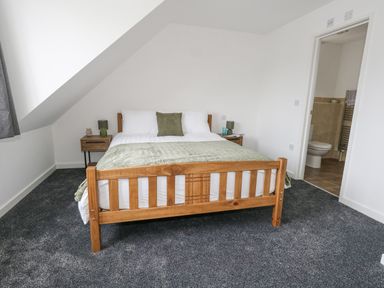 A bedroom with a wooden bed and green bedding next to two nightstands and an open door to a bathroom at Dotties Retreat in Weymouth