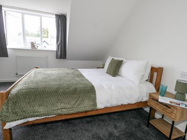 A bedroom with a wooden bed white bedding green throw and pillows beside a wooden nightstand with lamp and glass at Dotties Retreat in Weymouth