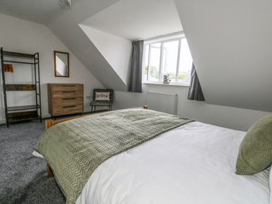 A bedroom with a bed green blanket a wooden dresser a chair and window at Dotties Retreat Weymouth