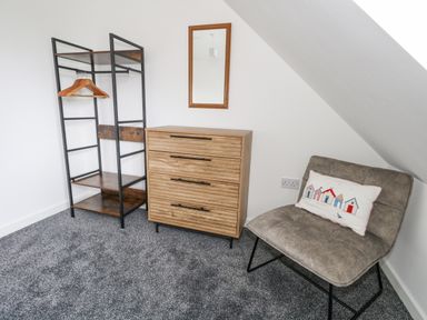 A corner of a room with a wooden chest of drawers a clothing rack with hangers and a gray chair with a cushion at Dotties Retreat in Weymouth