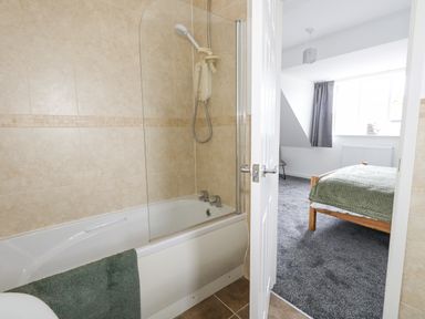 A bathroom with a bathtub and shower and a view into a bedroom with a bed and gray carpet at Dotties Retreat in Weymouth