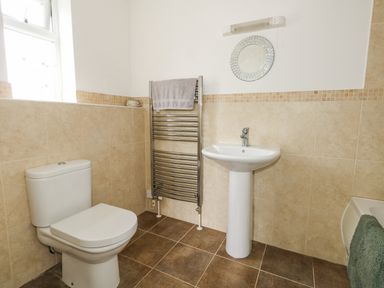 A bathroom with a toilet sink towel rack and circular mirror at Dotties Retreat in Weymouth