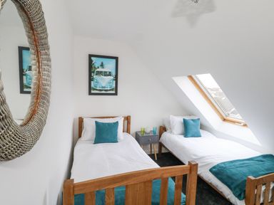 A bedroom with two single beds, a small table between them, a skylight window, and a mirror on the wall at Dotties Retreat in Weymouth