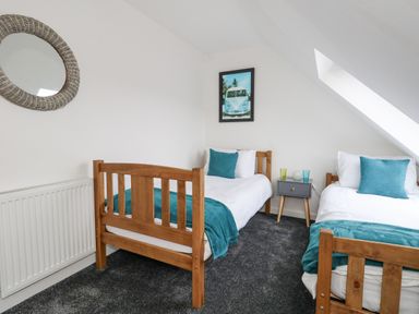 A bedroom with two single wooden beds with blue throws and cushions a bedside table with glasses and a framed picture on the wall at Dotties Retreat in Weymouth