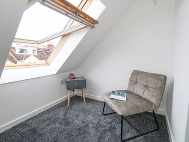 A small room with a gray chair and a blue side table under a skylight window at Dotties Retreat in Weymouth
