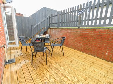 A backyard patio with wooden decking a round glass table with four black chairs and a wooden fence with a beach sign at Dotties Retreat in Weymouth