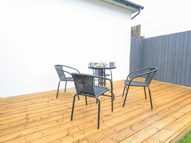 A wooden deck with a round table and three black chairs with cups on the table at Dotties Retreat in Weymouth