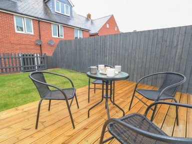 An outdoor patio with black metal chairs around a table with cups and snacks at Dotties Retreat in Weymouth