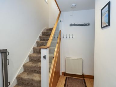 An entrance hallway with carpeted stairs wooden handrail coat hooks radiator framed picture and mat on wooden floor at The Swanage Rail Lookout in Swanage