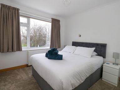 A bedroom with a large bed white bedding and rolled towels on top by a window with curtains at The Swanage Rail Lookout in Swanage