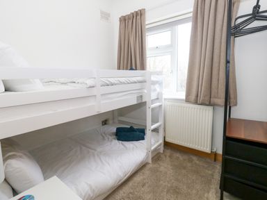 A bedroom with a white bunk bed a small window with beige curtains and a black clothes rack at The Swanage Rail Lookout in Swanage
