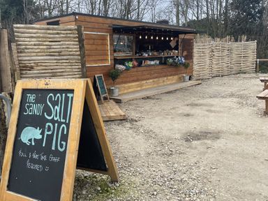 An outdoor wooden food stall with hanging lights and a blackboard sign advertising job vacancies at The Sandy Salt Pig