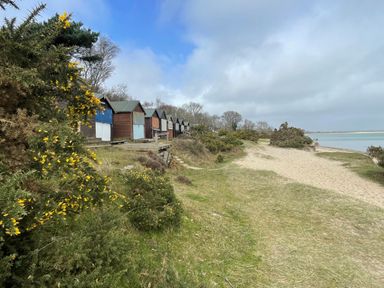 A row of small beach huts along a grassy path next to sandy shore and water at The Swanage Rail Lookout in Swanage