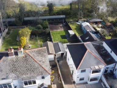 An aerial view of backyards with green lawns and garden structures behind houses at The Swanage Rail Lookout in Swanage