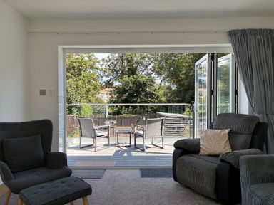 A living room with armchair and sofa leading to a patio at The Swanage Rail Lookout in Swanage