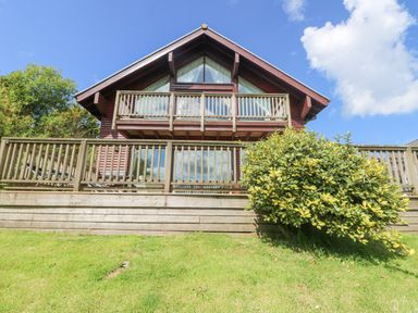 A wooden house with two balconies and a shrub in front at The Willows in Winnard's Perch near St Columb Major