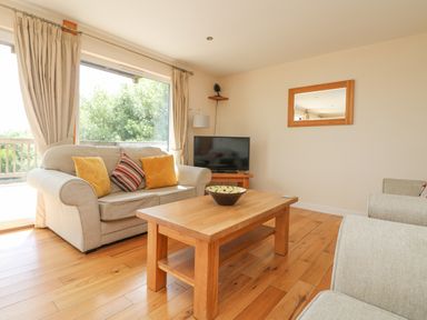 A living room with a sofa, armchairs, wooden coffee table, television, and mirror at The Willows in Winnard's Perch near St Columb Major