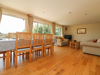 A dining area with a wooden table and chairs next to a living room with sofas and a coffee table at The Willows in Winnard's Perch near St Columb Major
