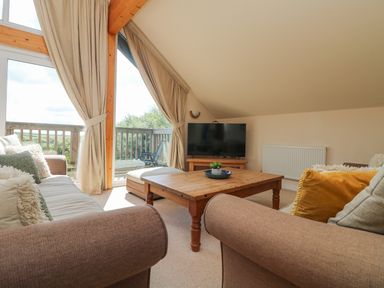 A living room with sofas a wooden coffee table a television and large windows at The Willows in Winnard's Perch near St Columb Major