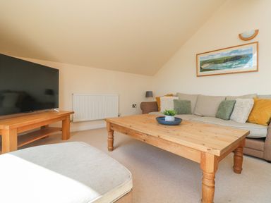 A living room with a wooden coffee table a large television on a wooden stand a sofa with cushions and a framed picture on the wall at The Willows Winnard's Perch near St Columb Major