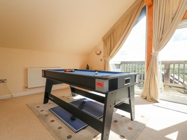 A game room with a pool table and a folded ping pong table near a window with curtains at The Willows in Winnard's Perch near St Columb Major
