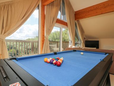 A pool table with balls arranged in a room with large windows curtains and a sofa at The Willows Winnard's Perch near St Columb Major