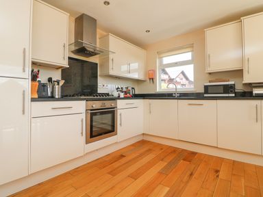 A kitchen with white cabinets a black countertop a stove an oven a microwave and a window at The Willows in Winnard's Perch near St Columb Major