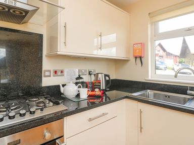 A kitchen corner with a gas stove oven white cabinets a kettle teapot and cups on the counter near a window at The Willows in Winnard's Perch near St Columb Major
